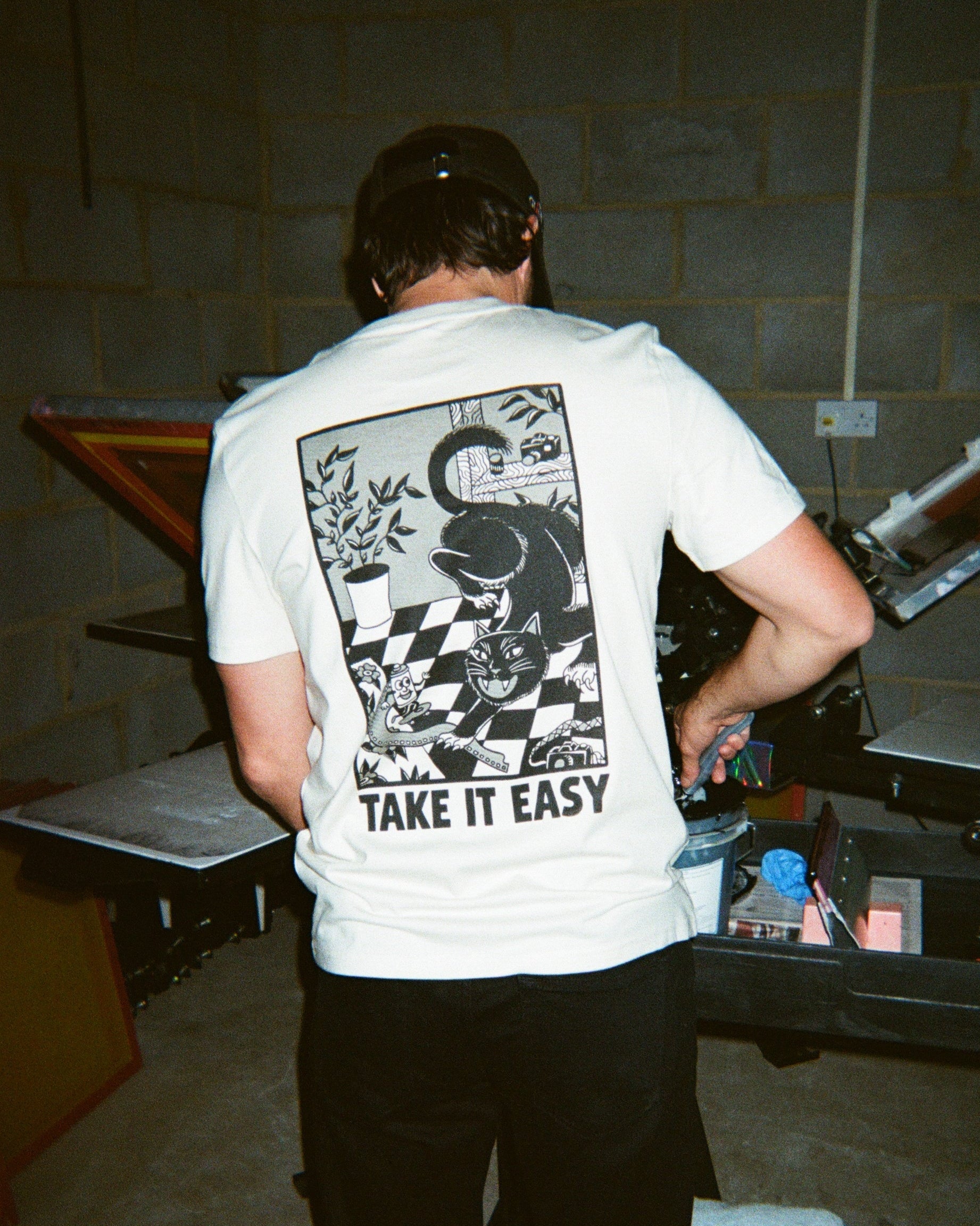 Person wearing a white t-shirt with a graphic design and text 'Take It Easy' in an indoor setting.