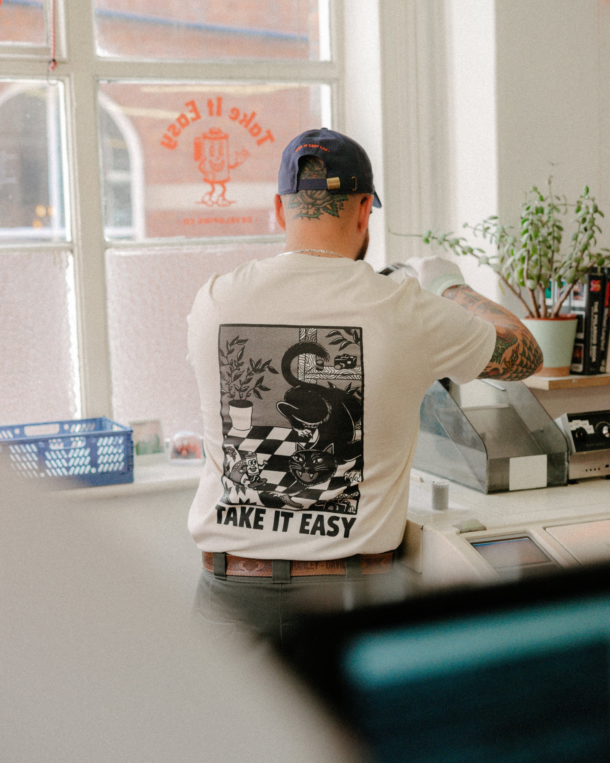 Person wearing a white t-shirt with a graphic design and text, sitting at a desk.