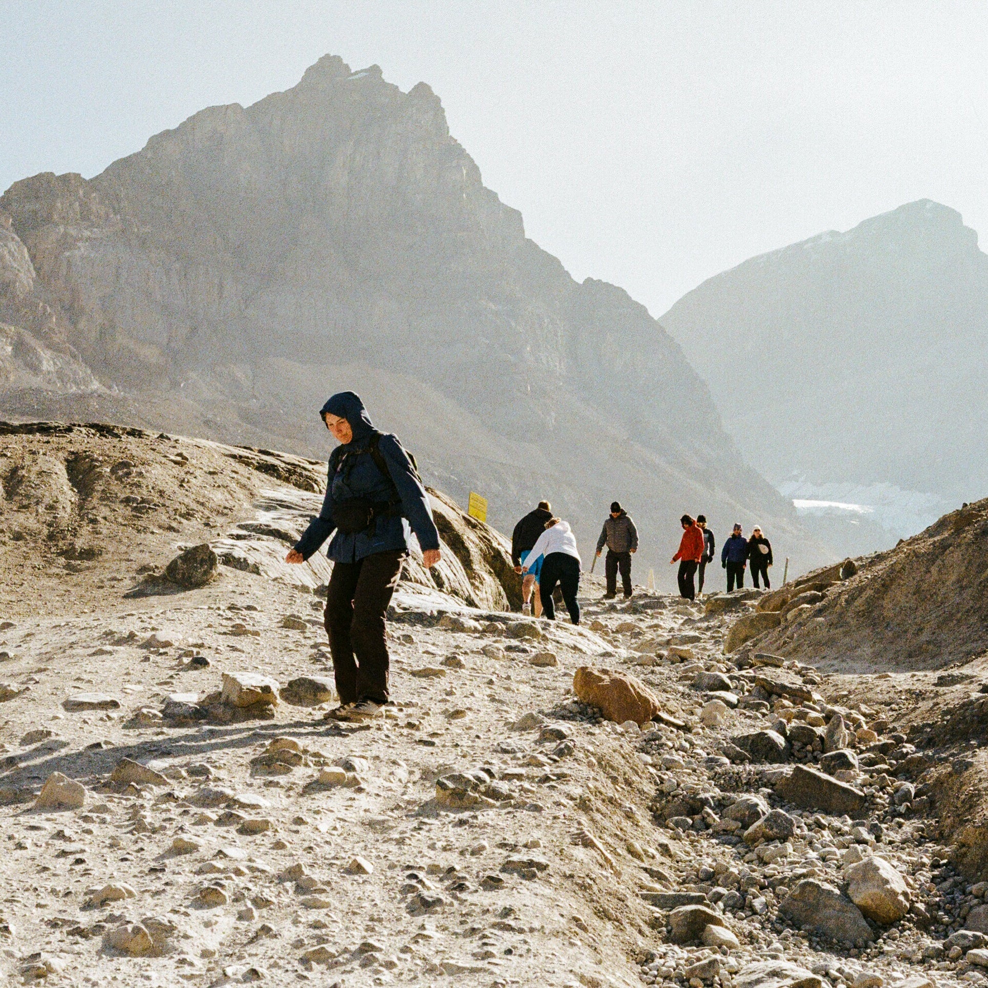 People hiking on a rocky mountain trail with snow-capped peaks in the background