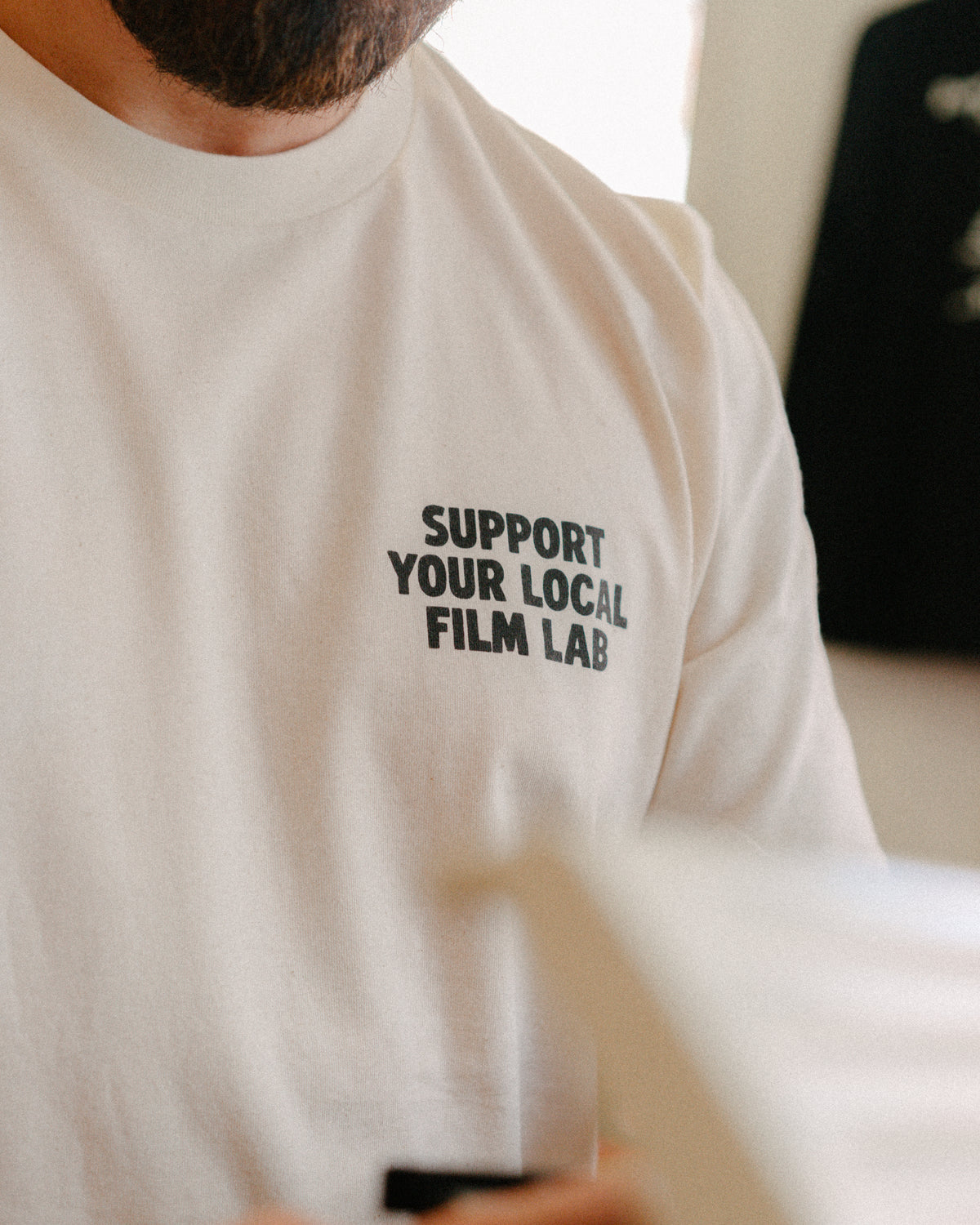 Person wearing a white t-shirt with 'Support Your Local Film Lab' text.